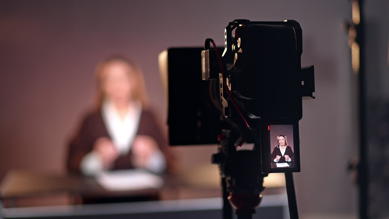Professional camera on tripod filming a female blogger. Lady with long hair talks on display.