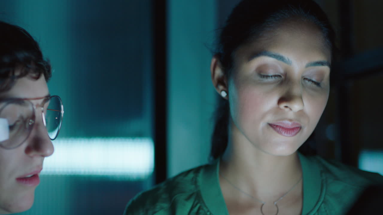 창의적인 비즈니스 팀이 늦게 일하고 태블릿 컴퓨터를 사용하는 동료들이 프로젝트에 대한 아이디어를 모으고 마감기간을 논의하고 헤드폰을 공유하는 여성이 밤에 사무실에서 회의를합니다.