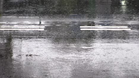 raindrops causing ripples, falling on reflective black tarmac road with white road markers