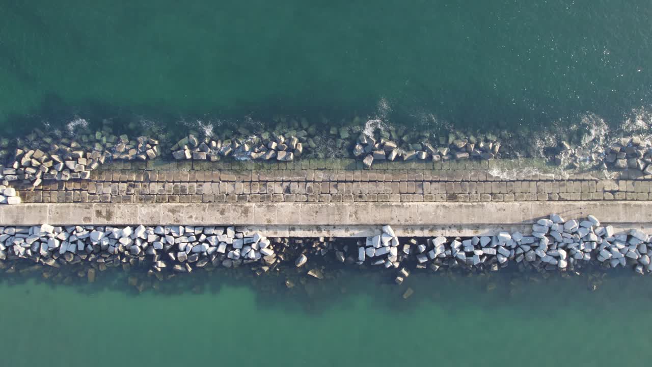 Aerial top down slider view Pier in the ocean with rocky stones, breakwater