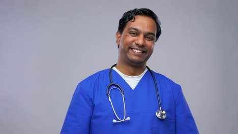 Happy-Indian-Male-Doctor-Showing-Thumbs-Up.healthcare,-profession-and-medicine-concept-happy-smiling-indian-doctor-or-male-nurse-in-blue-uniform-showing-thumbs-up-over-grey-background