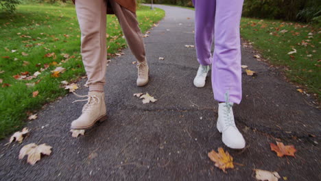 Two-women-walk-along-the-path-in-the-autumn-park,-walk-side-by-side,-only-the-legs-are-visible-in-the-frame.