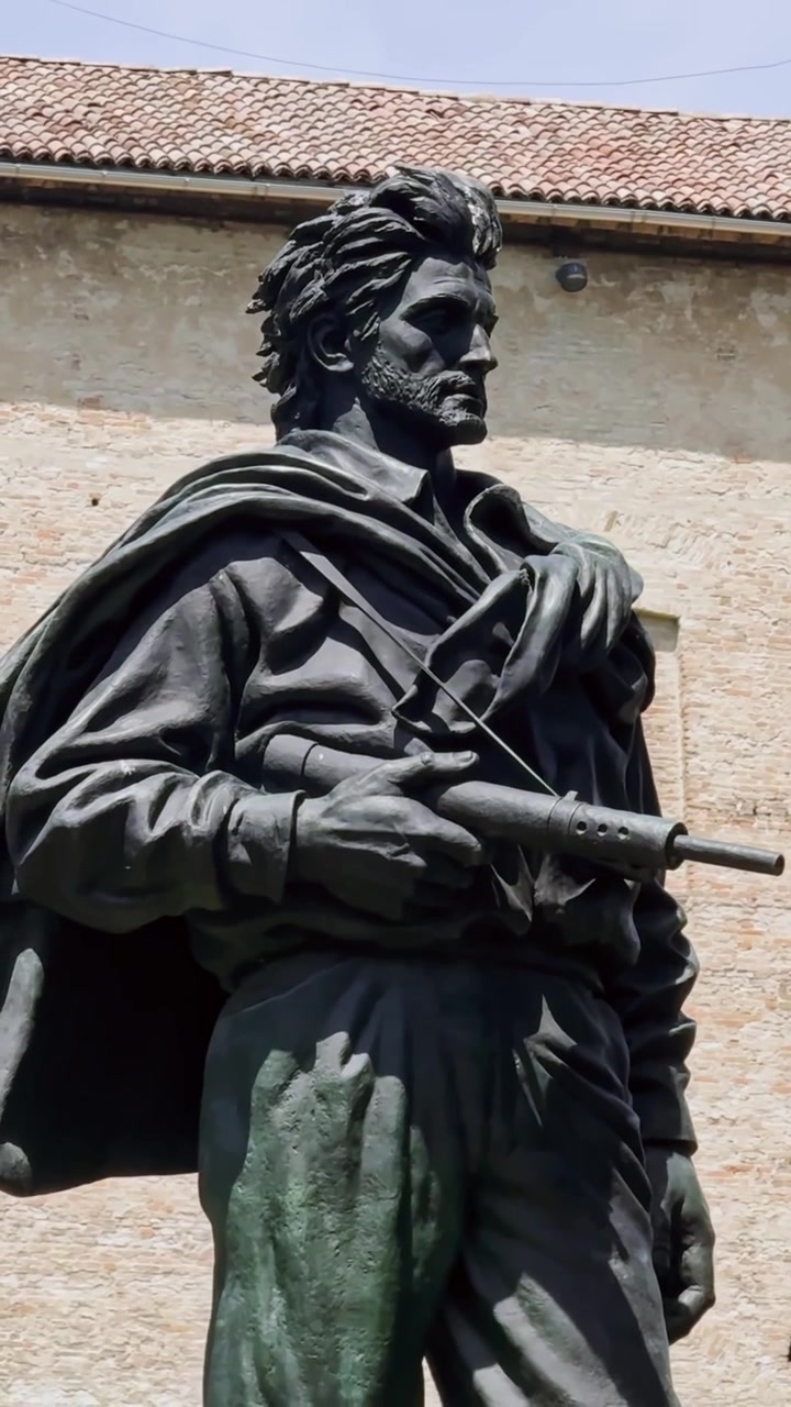Primo piano verticale del Monumento al Partigiano a Parma, Italia, che mostra un combattente della Resistenza italiana in bronzo con un mitra contro la muratura storica