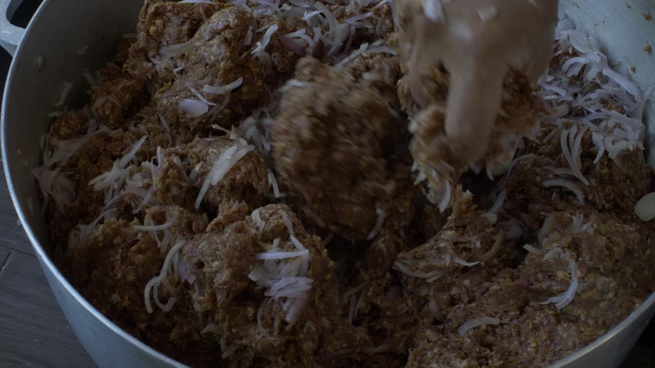 큰 팬 안에 다진 고기와 신선한 얇게 썬 양파를 손으로 반죽합니다