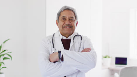 Retrato-En-Video-De-Un-Médico-Birracial-De-Pie-Con-Los-Brazos-Cruzados-Sonriendo-A-La-Cámara