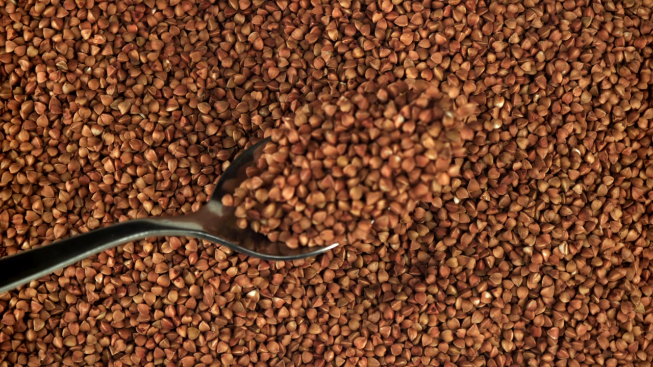 Versamento di grano saraceno da un cucchiaio con cambio di messa a fuoco