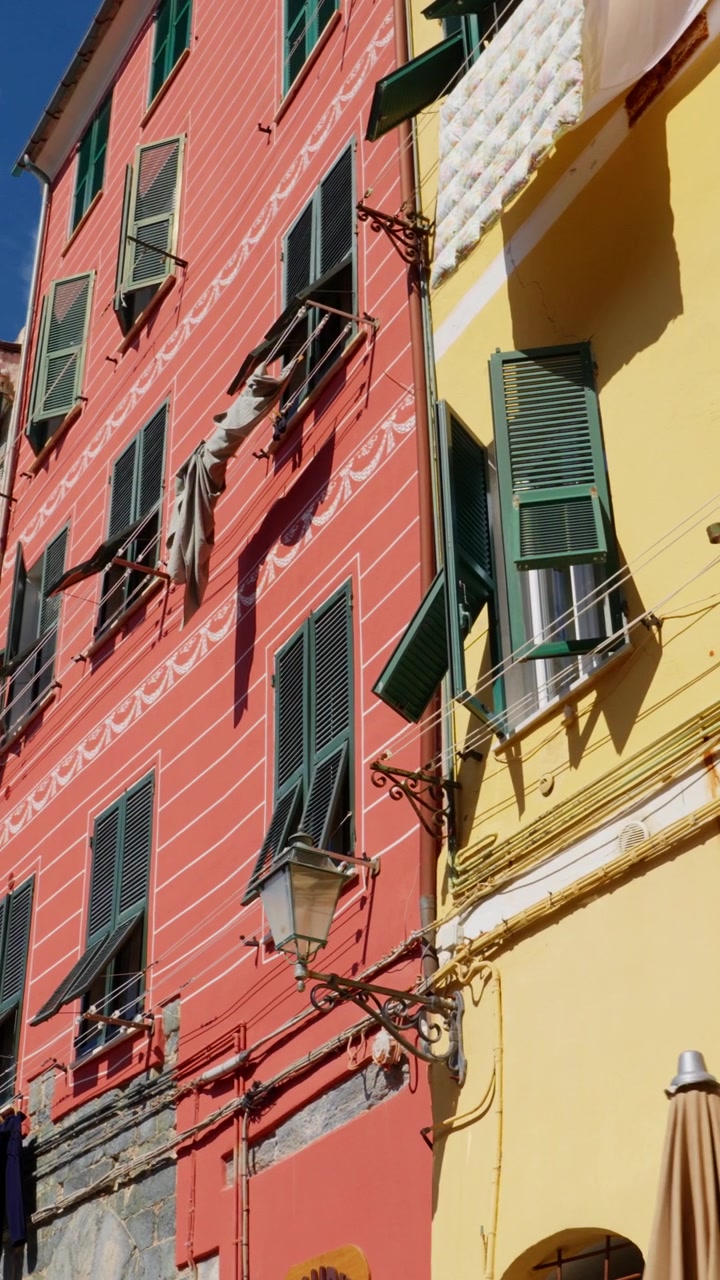 Ripresa panoramica verticale dal basso di facciate colorate con persiane e bucato steso a Vernazza, Cinque Terre