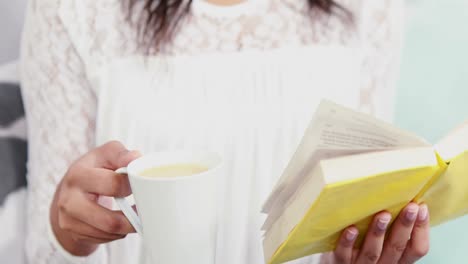 Woman-holding-a-mug-and-a-book-on-sofa-