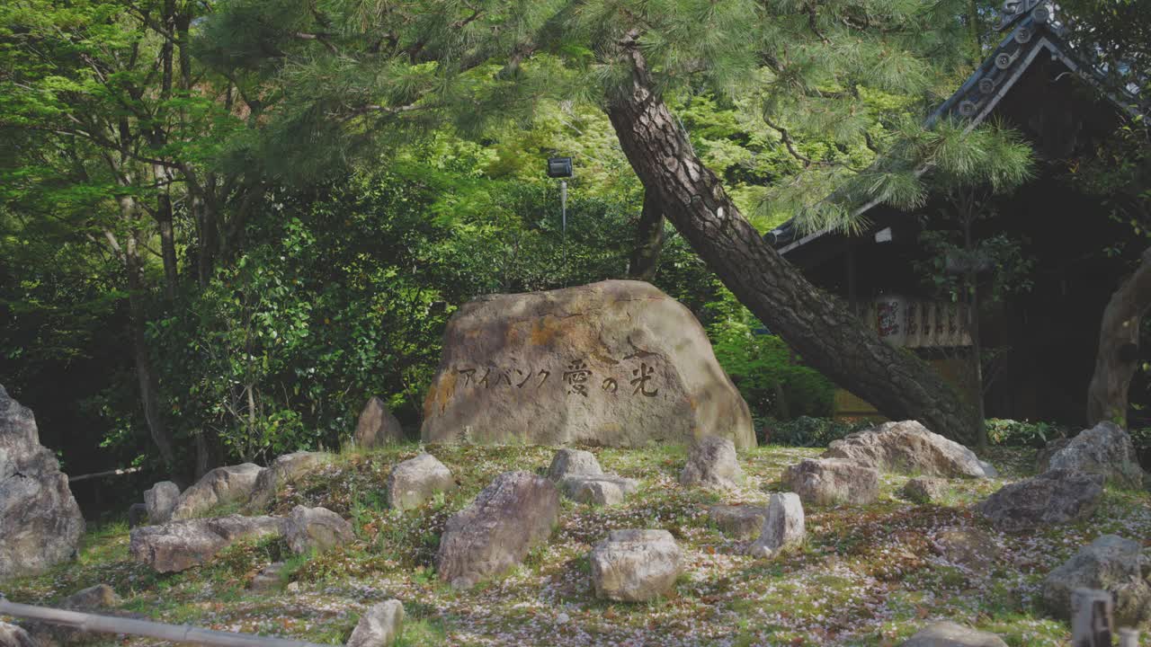 Calming garden view in Kyoto featuring a stone with Japanese inscription amid lush greenery. Perfect for themes of nature, culture, and tranquility.