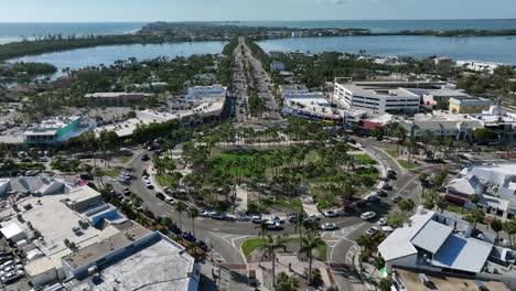 aerial view of st. armands circle in sarasota, showing vibrant shops, lush greenery and nearby waters. bustling roundabout is surrounded by scenic landscapes under a clear blue sky. sarasota, florida.