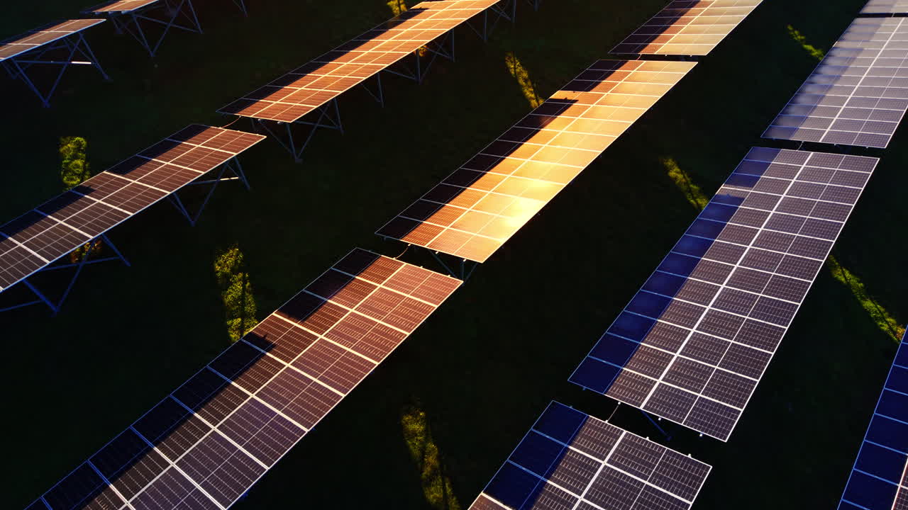 Vista dettagliata ad angolo elevato di pannelli solari con un potente bagliore solare arancione che si riflette sul vetro protettivo. Moduli fotovoltaici di sera