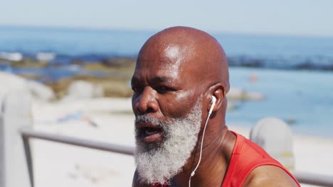 tired senior african american man wearing headphones taking a break from running on promenade