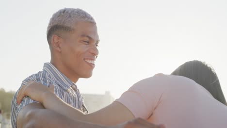 Happy-biracial-couple-embracing-on-promenade-by-beach,-in-slow-motion