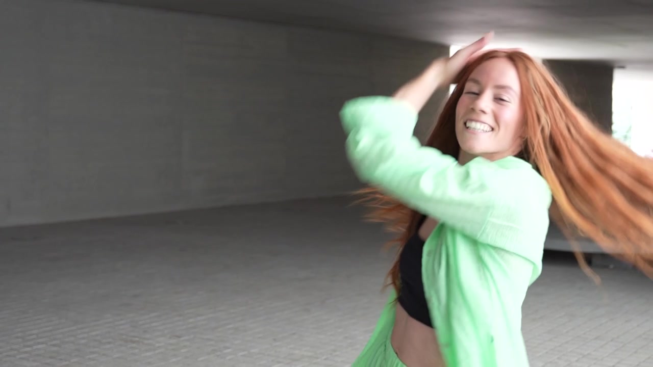A lady in a green suit dances confidently and freely in an urban corridor embodying joy and energy
