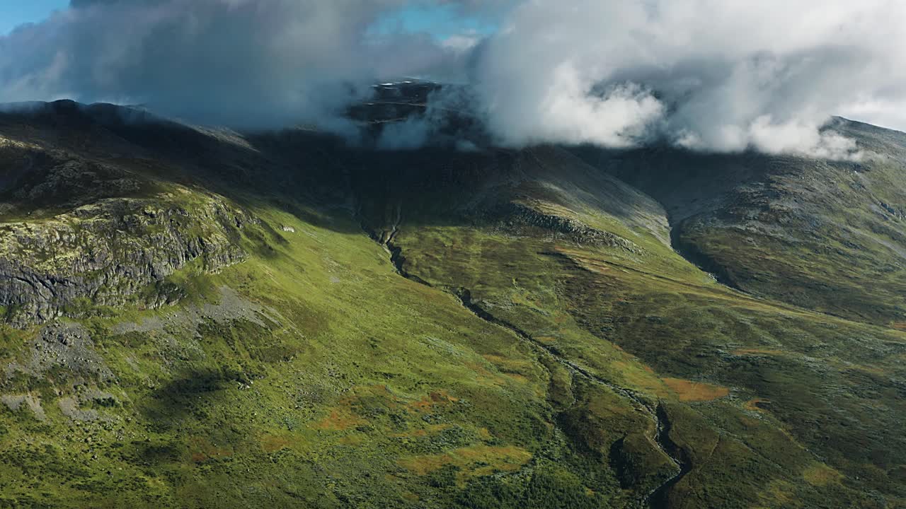 tomada de vuelo rápido de densas nubes blancas girando sobre las verdes colinas del noruega aurlandsfjellet