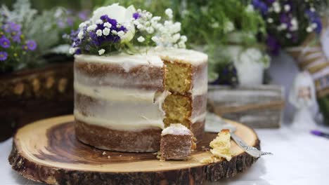 delicious eaten piece of decorative white icing wedding cake with flowers on top on celebratory day, close up pull back