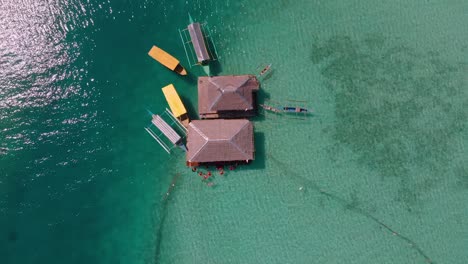 aerial drone shot on top view of villas in the middle of blue ocean with boats and people swimming