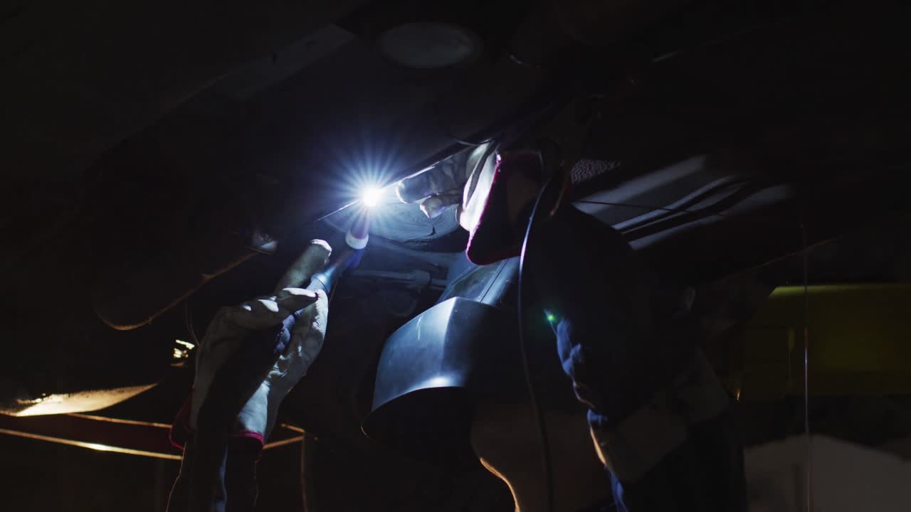 Female mechanic wearing welding helmet welding under a car at a car service station