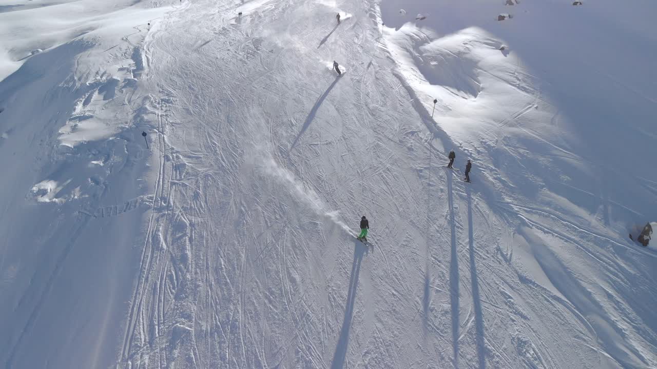 Aerial drone view of skiers, downhill skiing down snowy slopes in the sunny alps - tilt, drone shot