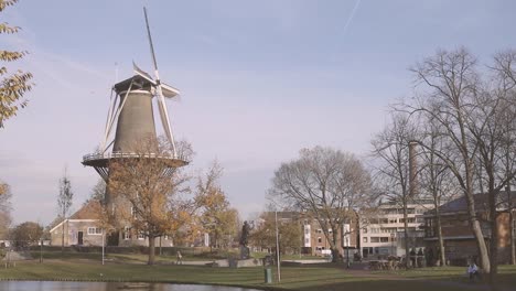 Molino-De-Viento-Típico-Holandés-Con-Mechas-Girando-En-Una-Zona-Residencial-De-La-Ciudad-De-Leiden,-Países-Bajos,-En-Otoño-Con-árboles-Casi-Sin-Hojas