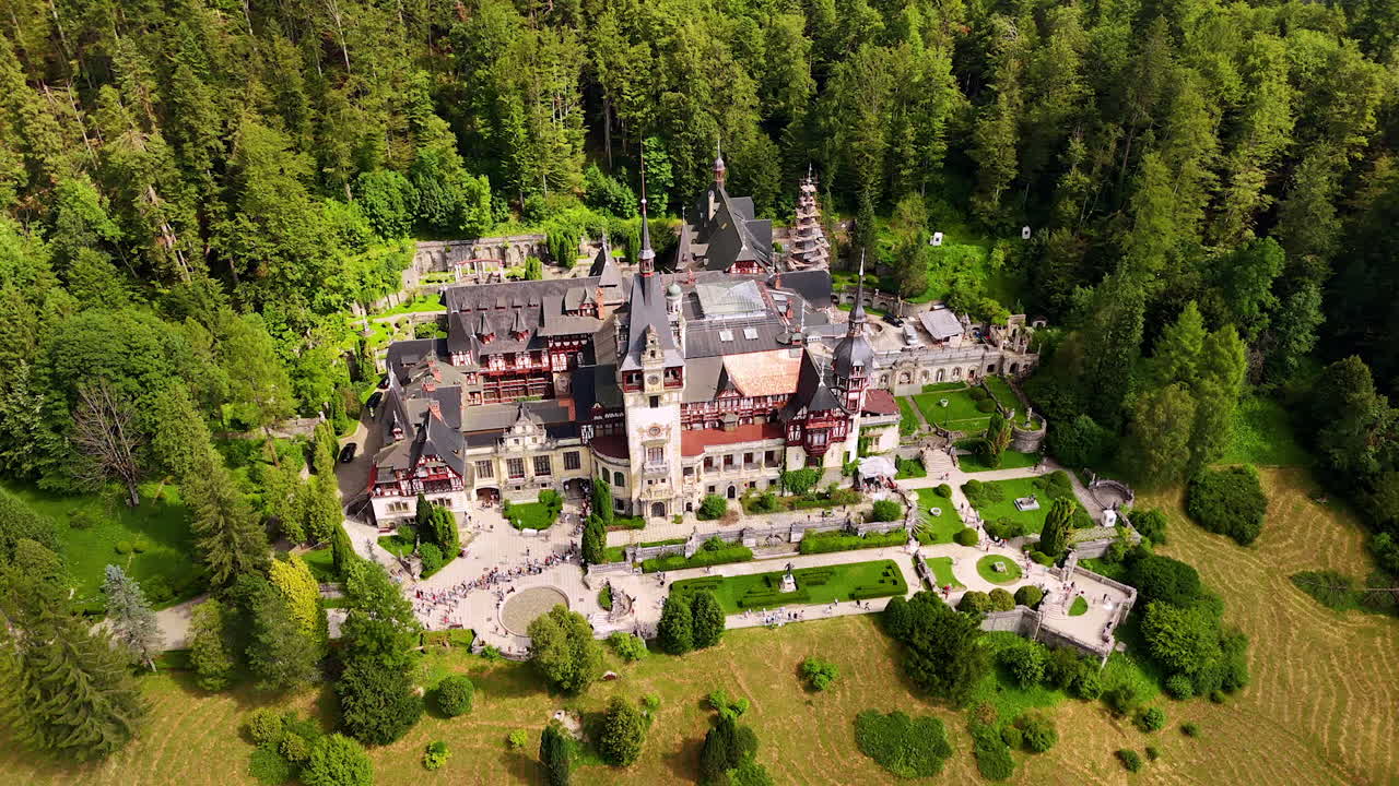 Beautiful scenery of the Peles Castle in Prahova County, Romania. Lush green pine tree wood grows around. Aerial view
