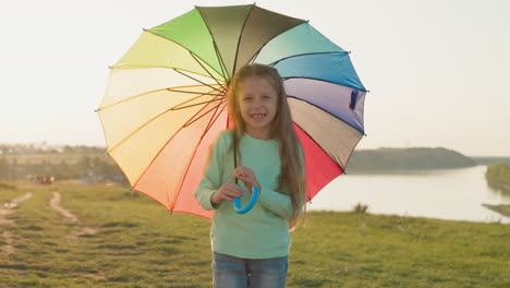 girl swirls colorful umbrella against river parasol catches sunlight casting highlights of colors