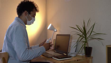 a man using laptop and applying alchohol in his hands to prevent corona virus - mid-shot