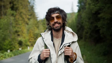 portrait of a brunette tourist guy in big yellow glasses in a special uniform for tourists who poses and looks at the camera near the road against the backdrop of a mountain forest