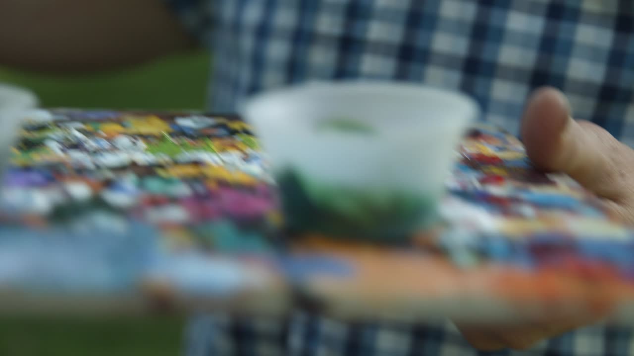 화가는 다시 칠할 준비가 된 녹색 페인트가 담긴 화가의 팔레트에 붓을 담근다