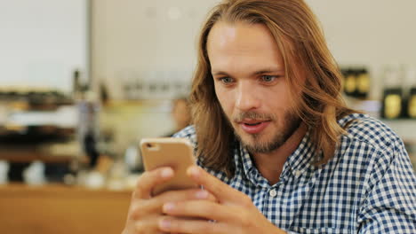 close-up view of caucasian blond man with long hair texting on the phone sitting at a table in a cafe