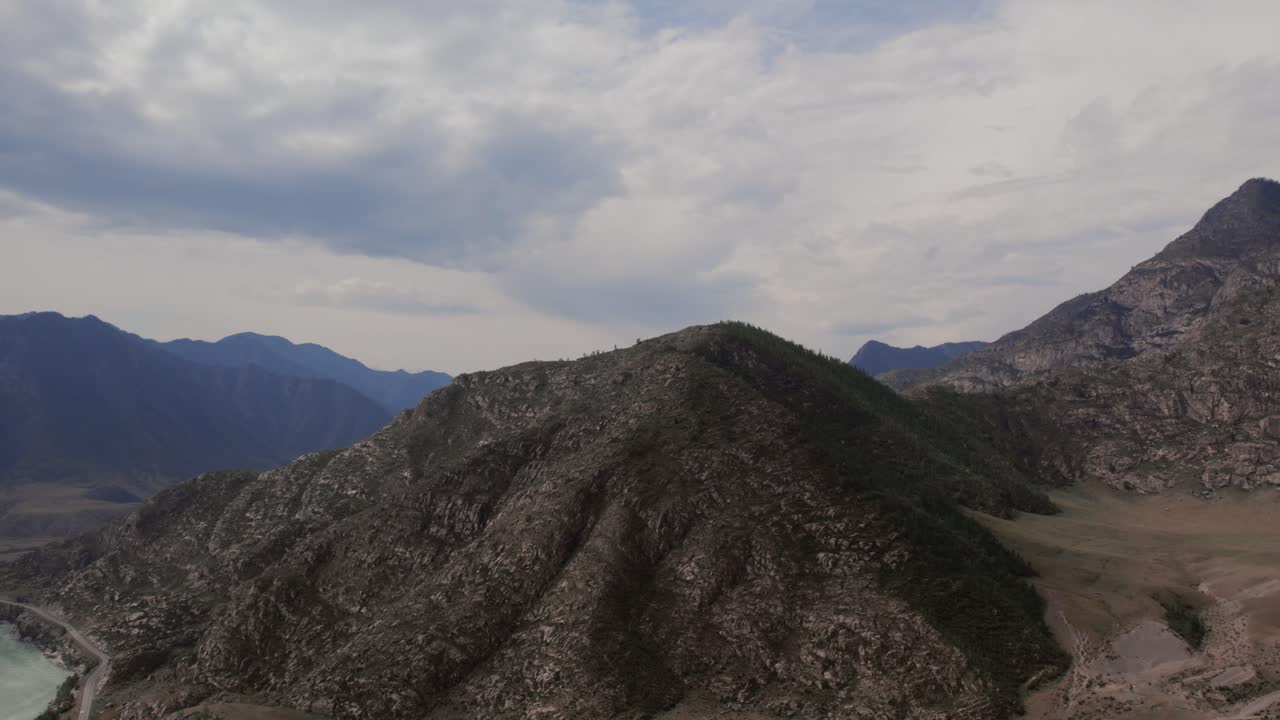 Vista de dron de una cresta montañosa rocosa y una carretera sinuosa a lo largo de la Carretera Chuysky en la República de Altái, Rusia, bajo un cielo nublado dramático, escena de viaje por una naturaleza salvaje remota