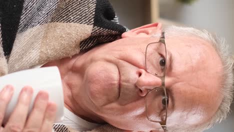 grandfather in glasses is drinking tea he has a cold and a runny nose vertical video