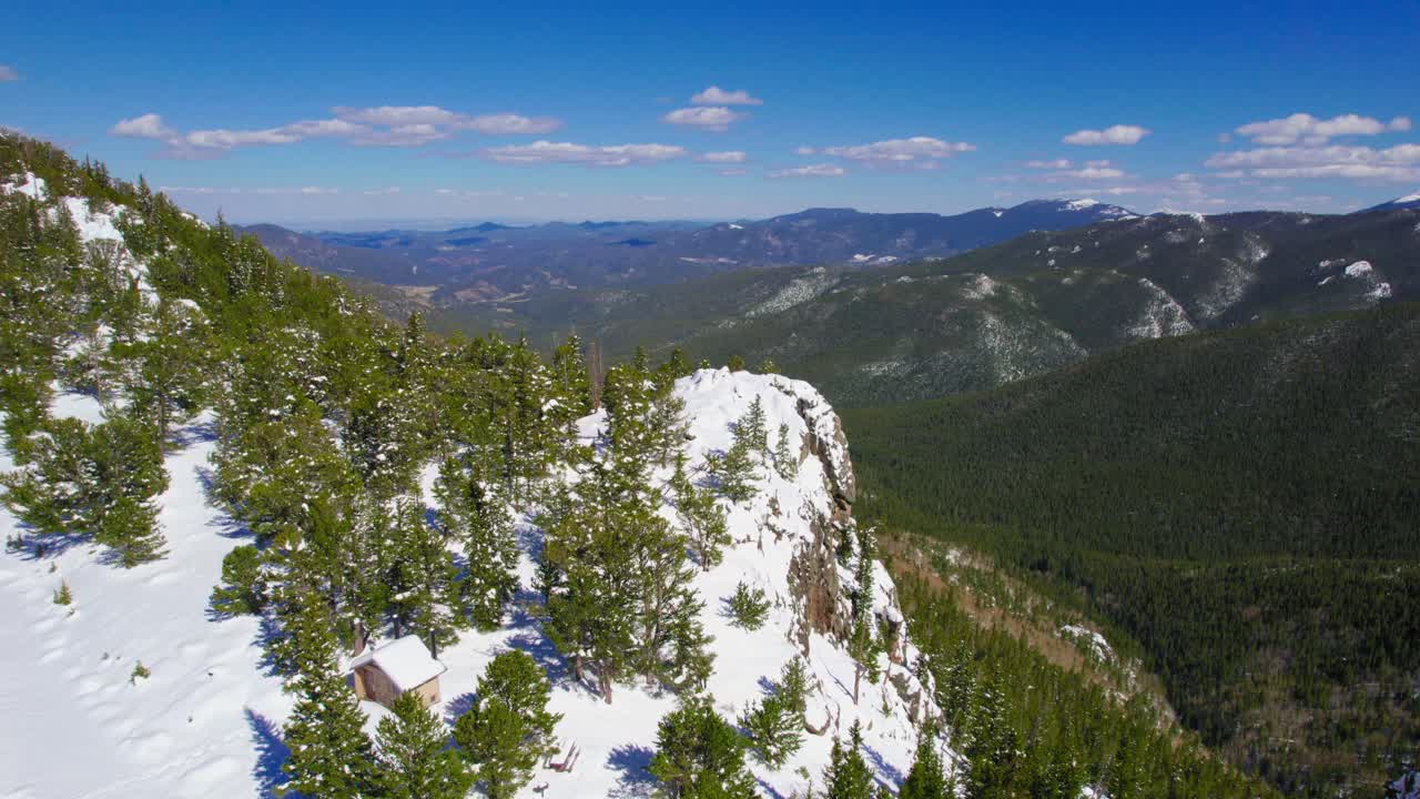 toma aérea de un gran acantilado rocoso cubierto de nieve que cuelga sobre un exuberante bosque alpino verde y abierto valle de montaña en las montañas rocosas monte evans colorado ee.uu.