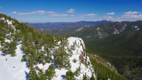 aerial shot of large snow covered rocky cliff hanging over wide open lush green alpine forest mountain valley in rocky mountains mount evans colorado usa