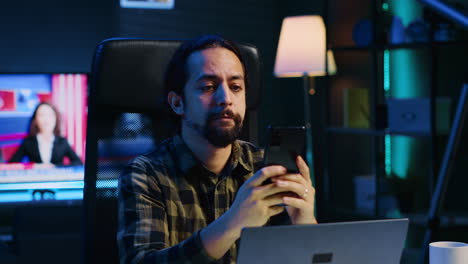 Man-relaxing-in-apartment-sitting-at-office-desk,-texting-friends