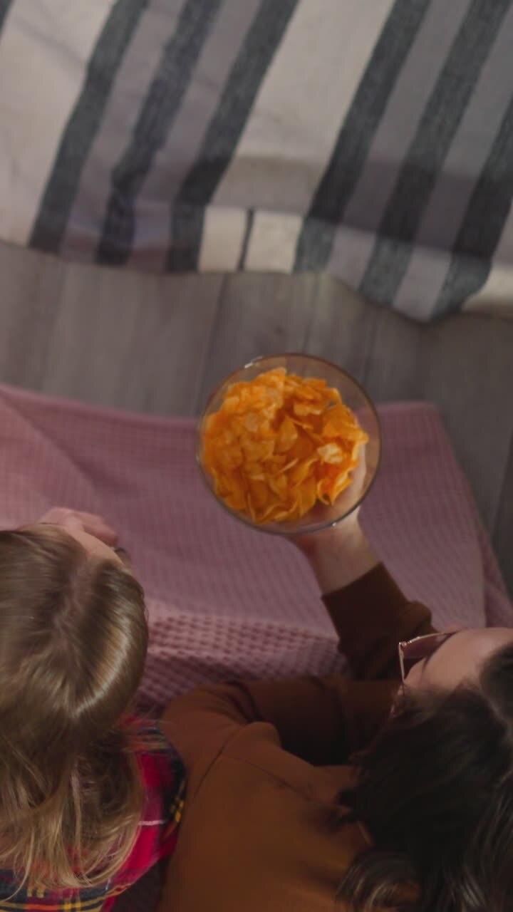 Cute young friends drink beer and eat chips watching TV series at home upper view slow motion. People spends time together at cinema evening