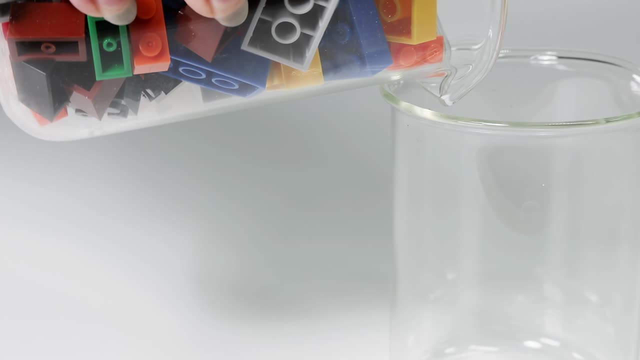 Hands carefully pour vibrant plastic blocks from one glass container to another, showcasing precision and color variety.