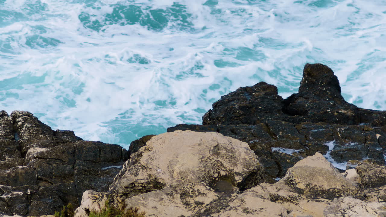 Onde marine si infrangono sulla costa rocciosa formando schiuma e nebbia