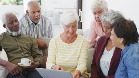 personas mayores felices y diversas hablando y usando computadoras portátiles en el hogar de ancianos