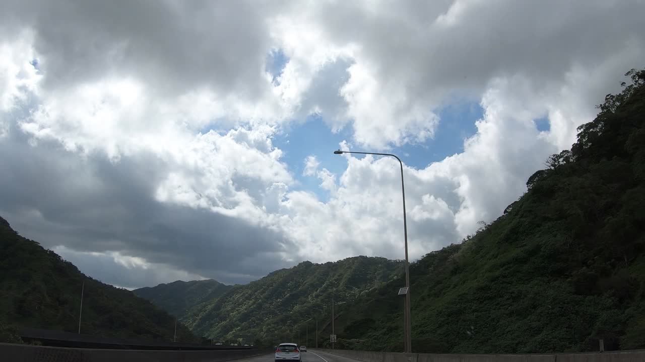흐린 하늘과 고속도로 양쪽의 숲이있는 고대 사화산을 가로 질러 오아후를 통해 운전