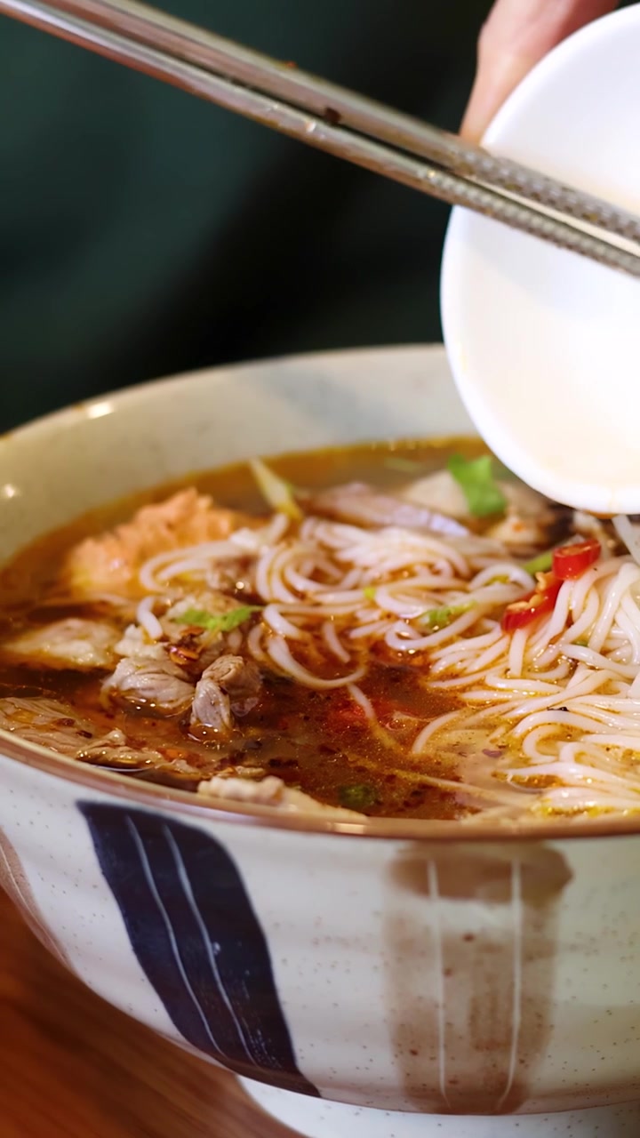 Cận cảnh đôi tay thêm ớt thái lát vào một bát phở bò nóng hổi.