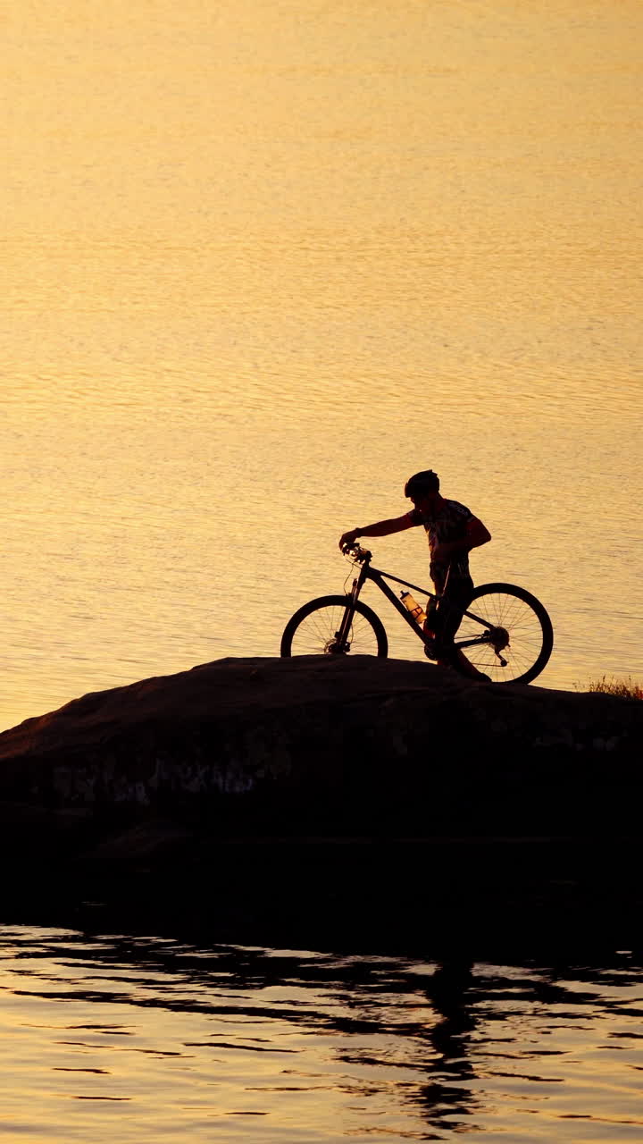 Cyclist in helmet and glasses with his bike near the water. Professional bicyclist comes to the river and washes his hands in water in the evening. Vertical video