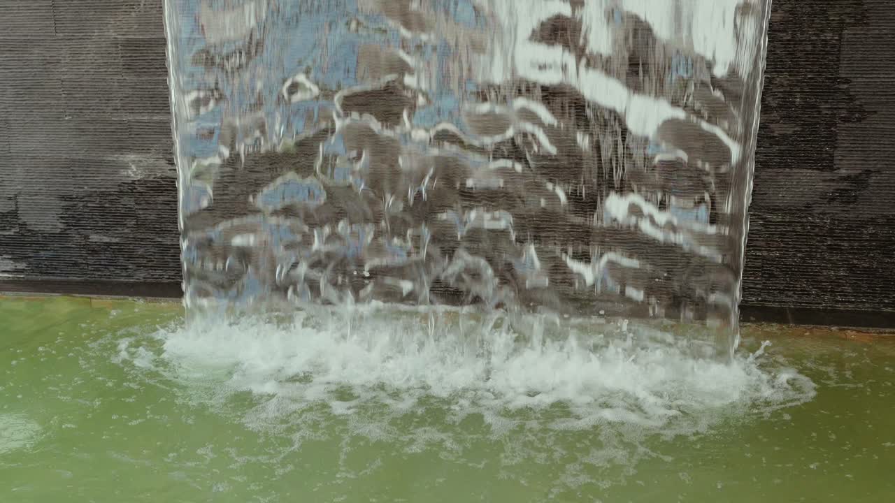 waterfall feature with textured backdrop splashing into a green pool