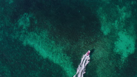 top down aerial view of a speedboat riding through shallow blue waters