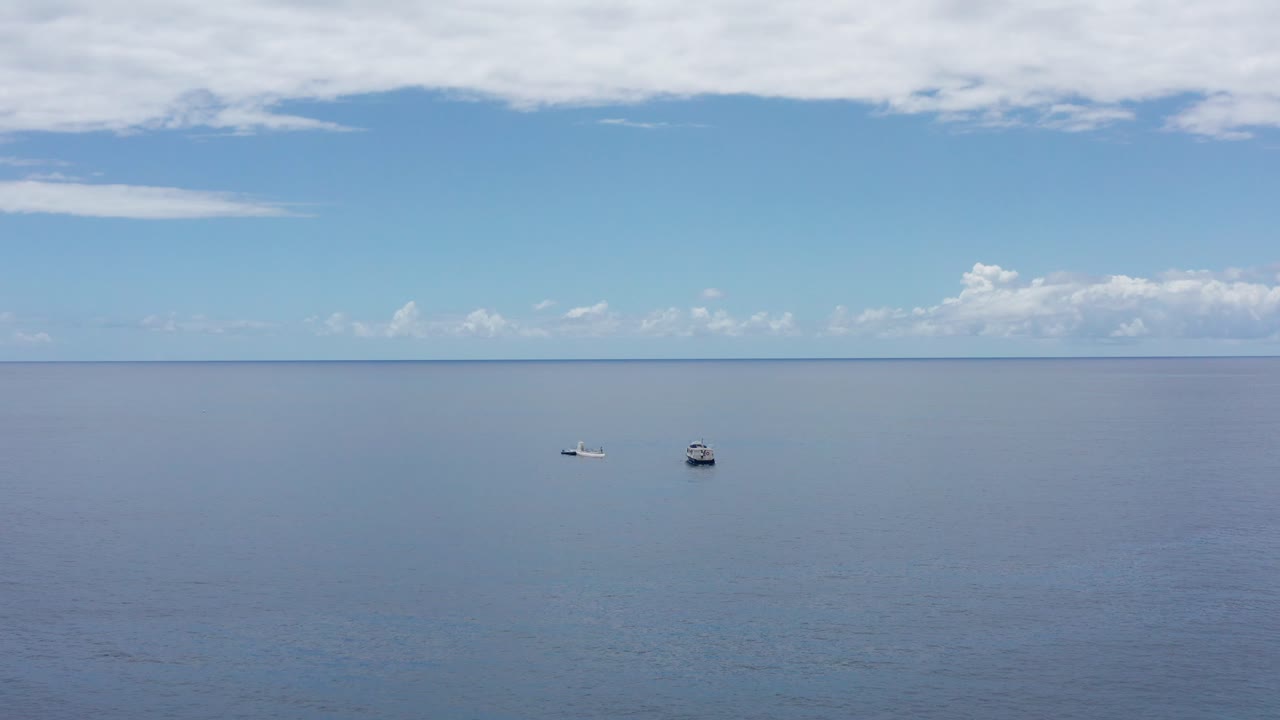 Aerial wide push-in shot of a small ferry boat approaching a submarine in the open ocean off the coast of Kailua-Kona, Hawai'i