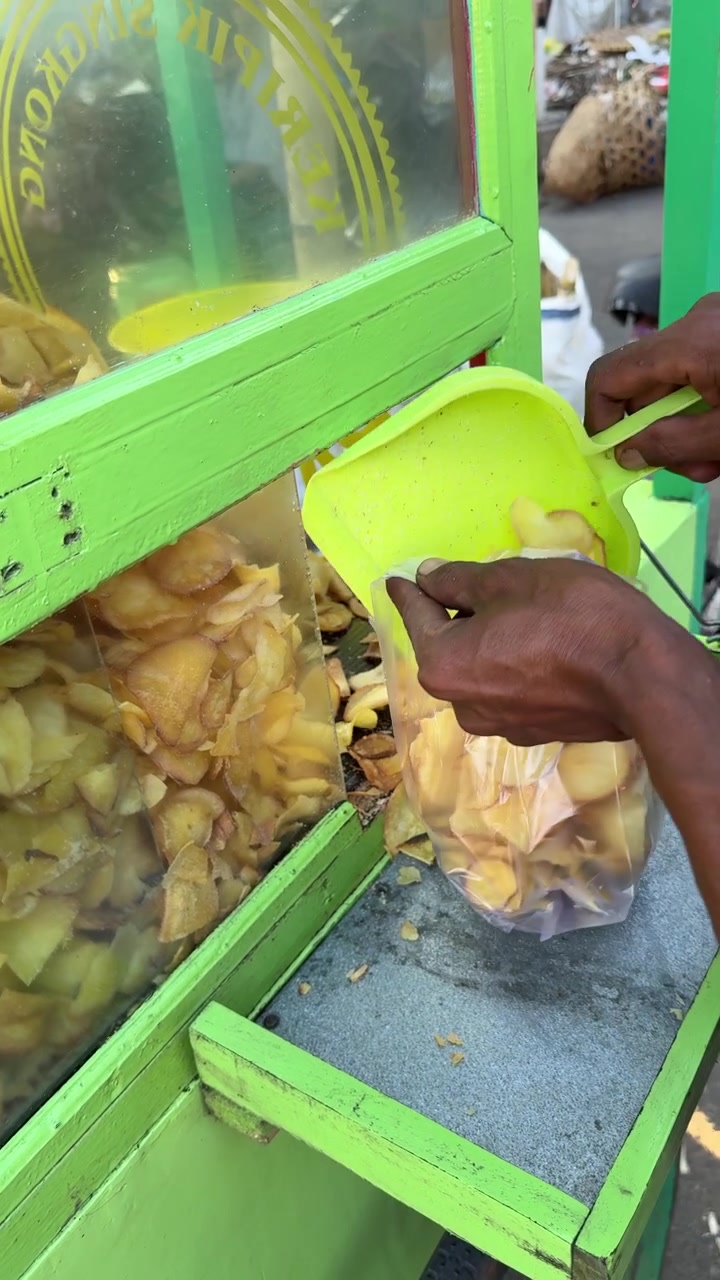 Venditore che serve e confeziona chips di manioca in una bancarella di street food
