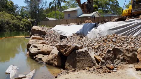 una excavadora que utiliza un agarrador de rocas para construir un muro de rocas a lo largo de un río