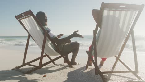 smiling senior african american couple lying on sunbeds on sunny beach