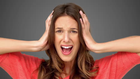 frustrated woman holding her head between hands on grey background