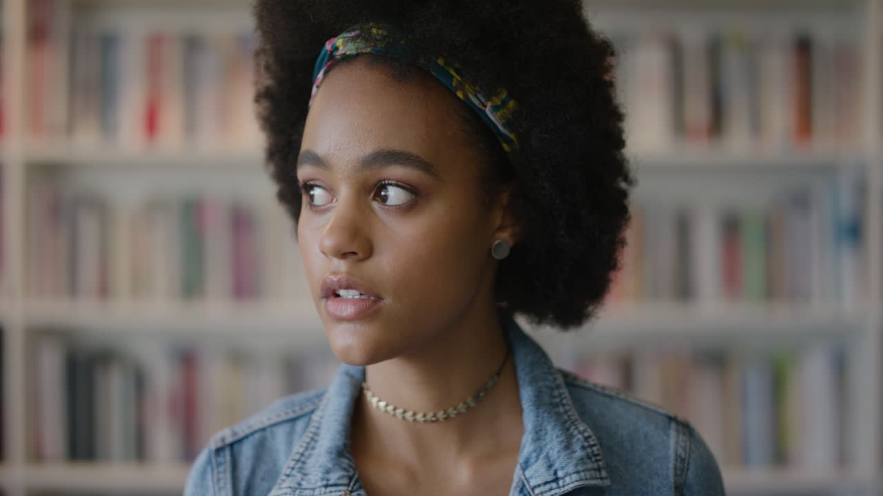 ritratto bella giovane donna afroamericana studentessa che si guarda attorno pensosa contemplativa sorridente felice con acconciatura afro slow motion scaffale sfondo